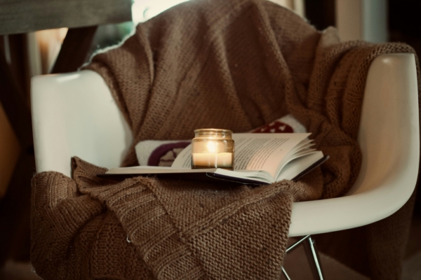Gemütlicher Sessel mit Decke, Buch und Kerze im Abendlicht, Entspannung mit ätherischen Ölen bei DOLLART DROPS