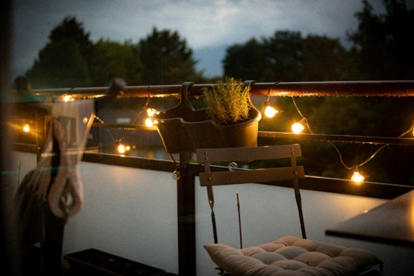 Gemütlicher Balkon am Abend mit Lichterkette und Kräutertopf, Duftstimmung für draußen